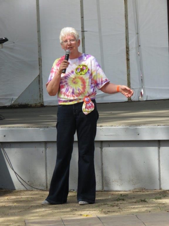A woman in a tie dye shirt is speaking into a microphone