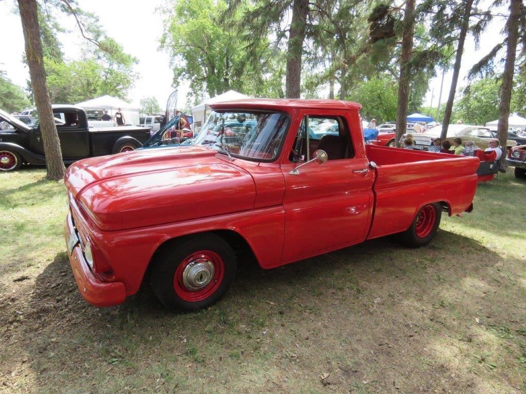 A red truck is parked in the grass at a car show.