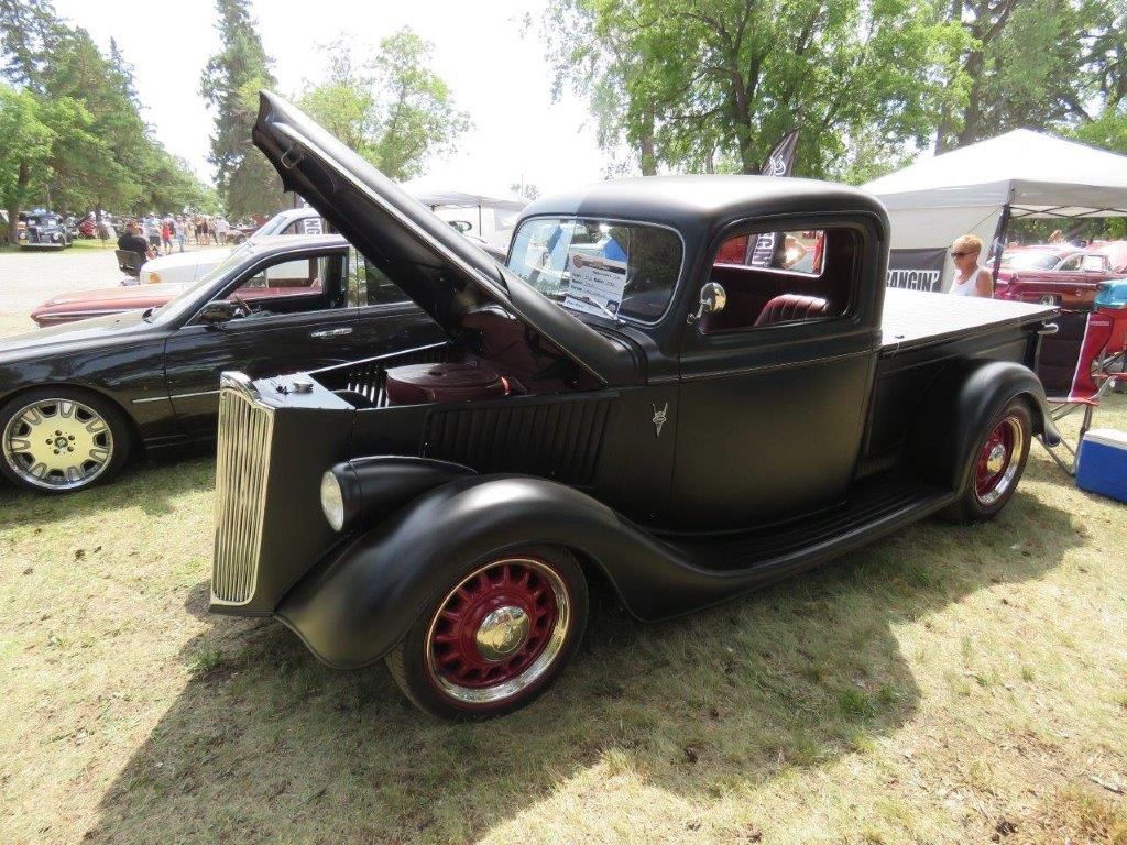 A black truck with the hood up is parked next to a black car.