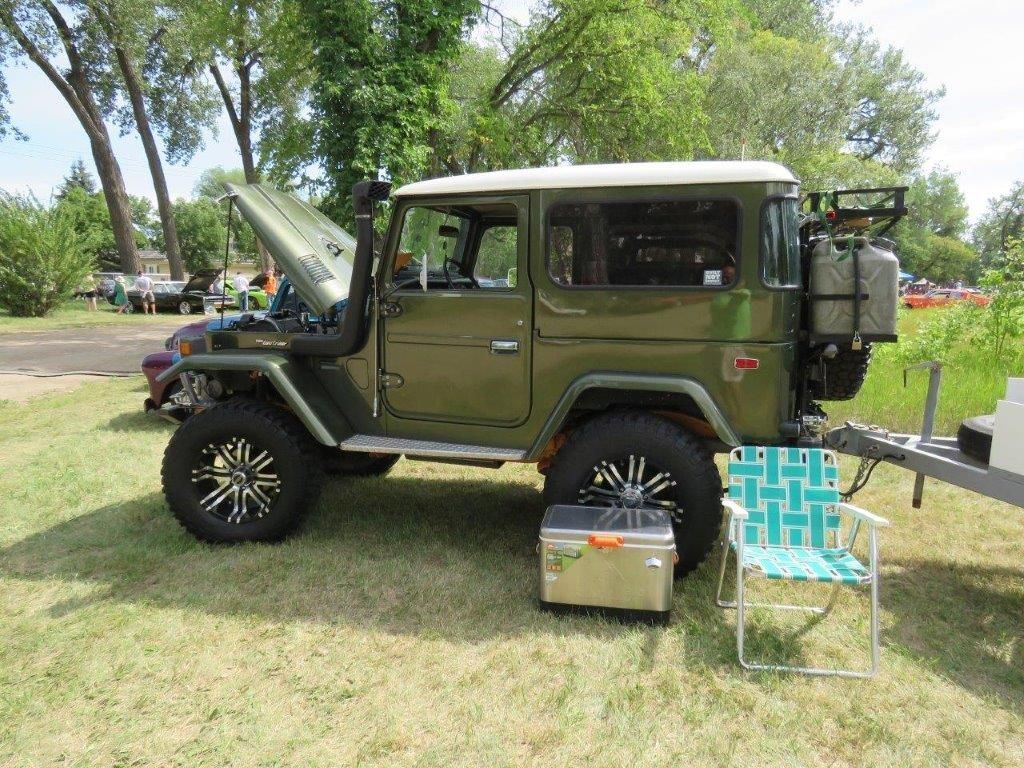 A green jeep is parked on the grass next to a chair and a cooler.
