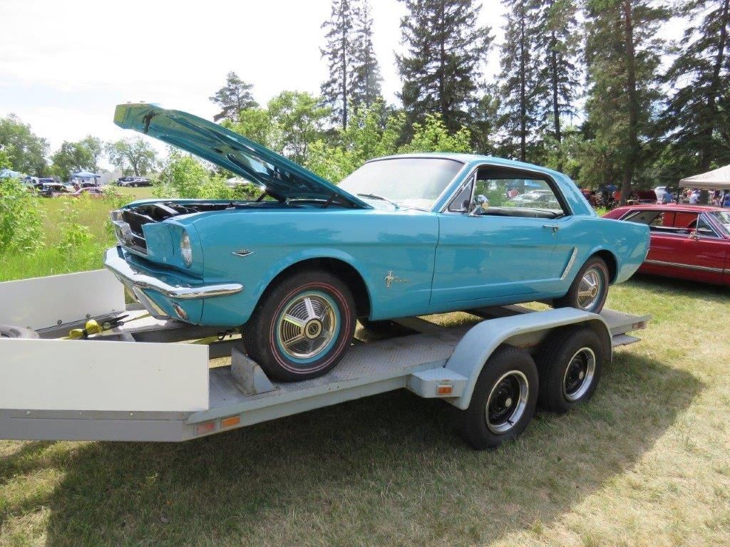 A blue mustang is on a trailer at a car show.