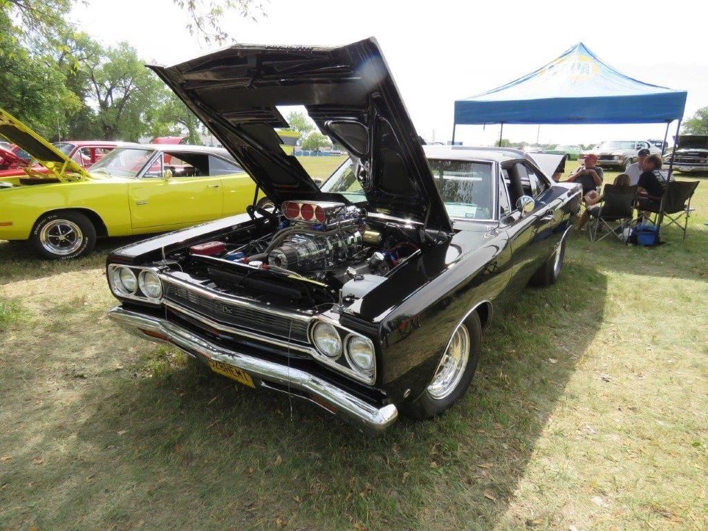 A black car with the hood up is parked in the grass at a car show.