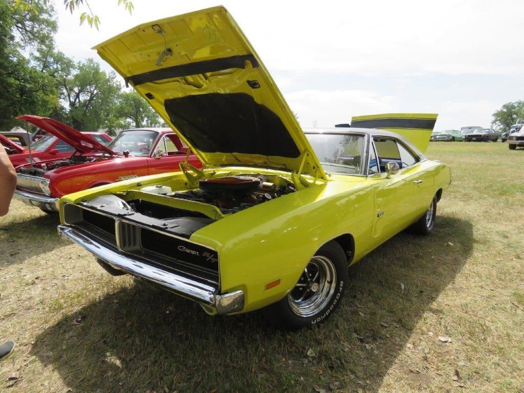 A yellow dodge charger with the hood up is parked in a field.