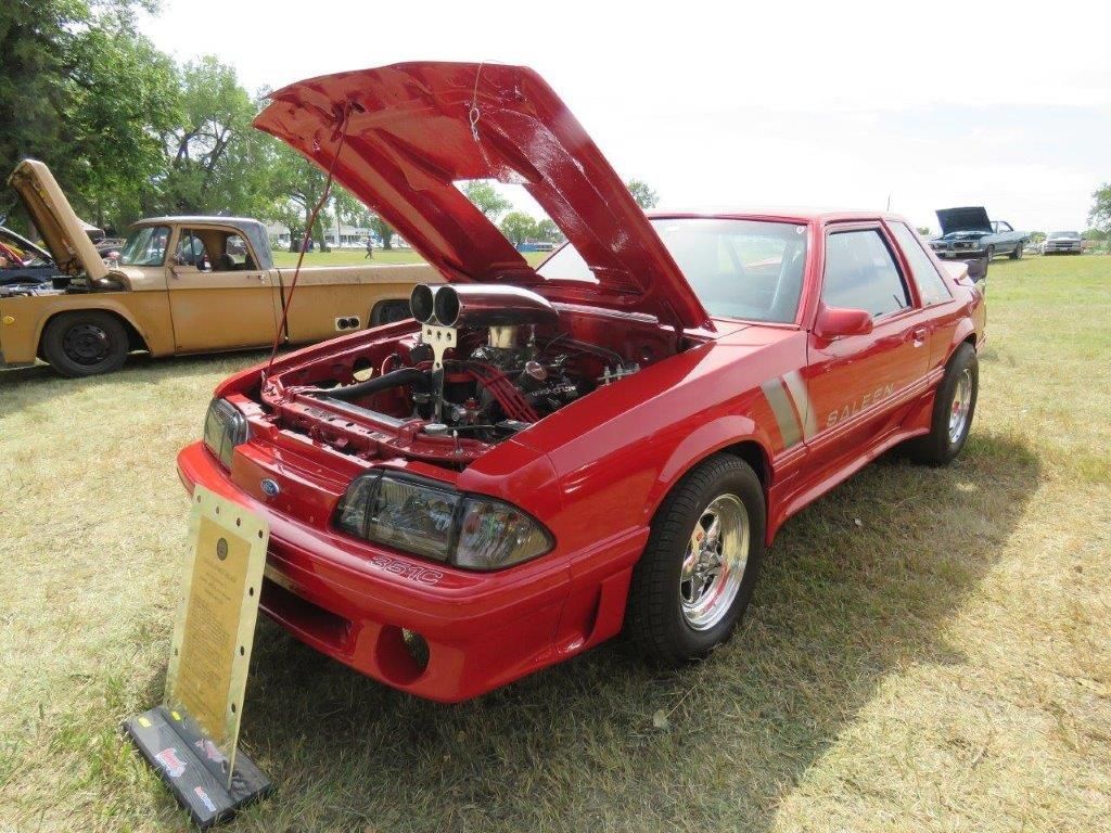 A red car with the hood up is parked in a grassy field.