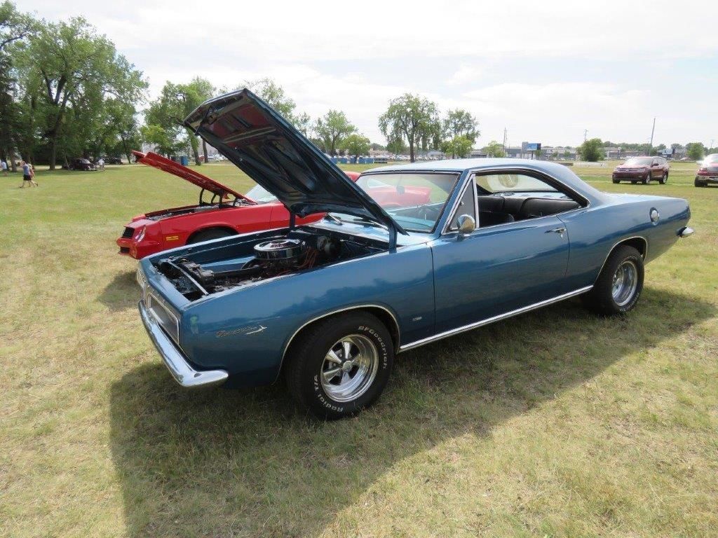 A blue car with the hood up is parked in a grassy field.