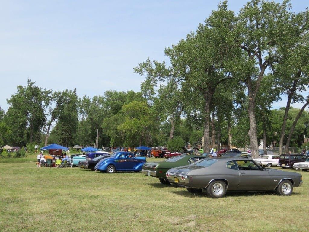 A row of cars are parked in a grassy field.