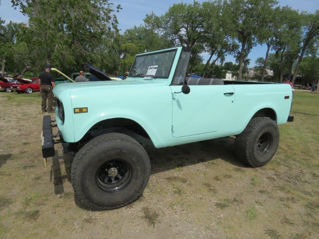 A light blue jeep is parked in a grassy field.