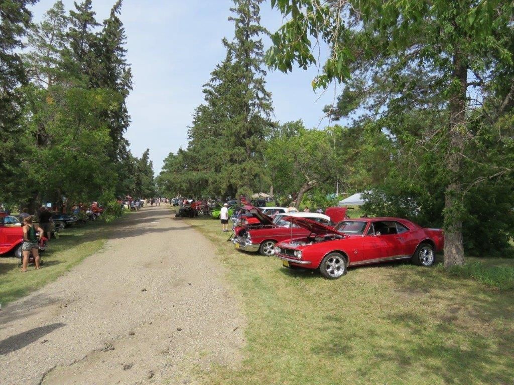 A row of red cars are parked on the side of a dirt road.