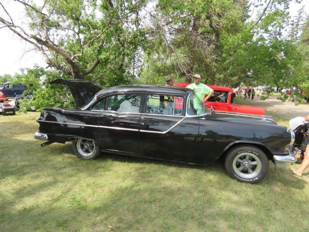 A black car is parked in a grassy field at a car show.