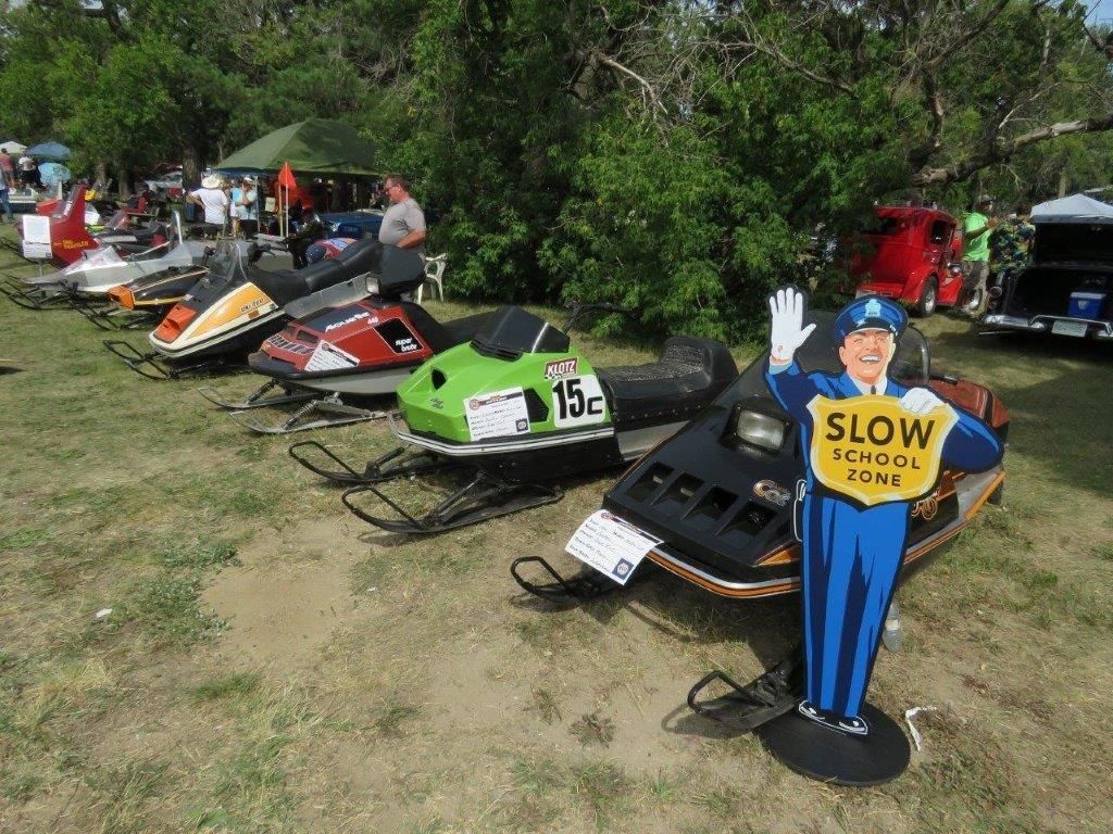 A row of snowmobiles are parked next to a sign that says slow school zone