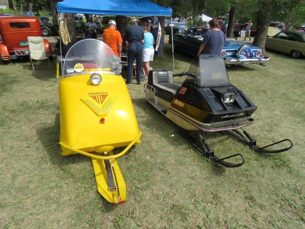Two yellow snowmobiles are parked next to each other in a grassy field.