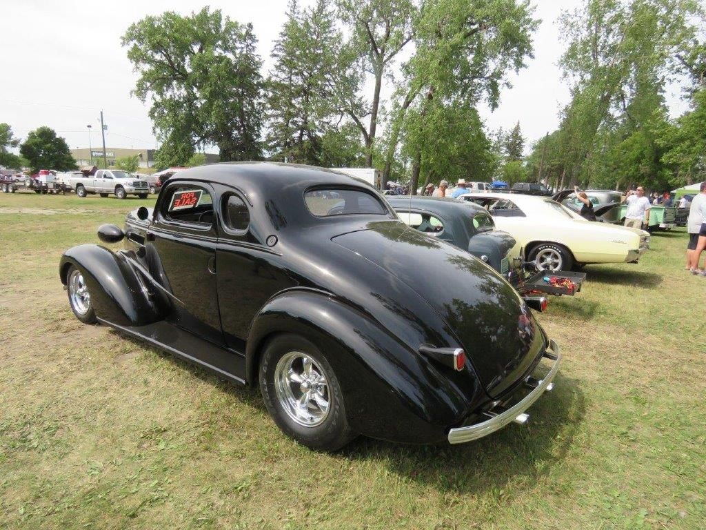 A black car is parked in a grassy field at a car show.