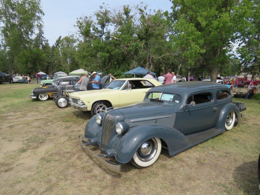 A row of old cars are parked in a grassy field.