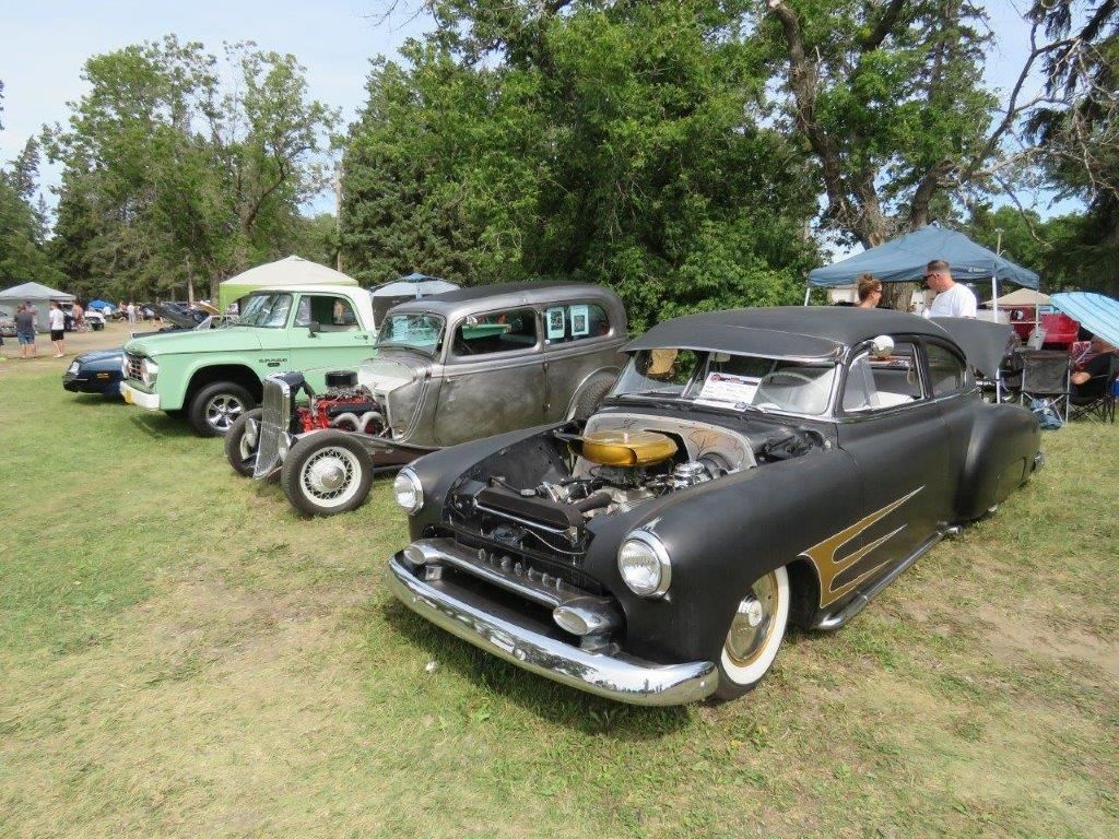 A row of old cars are parked in a grassy field.