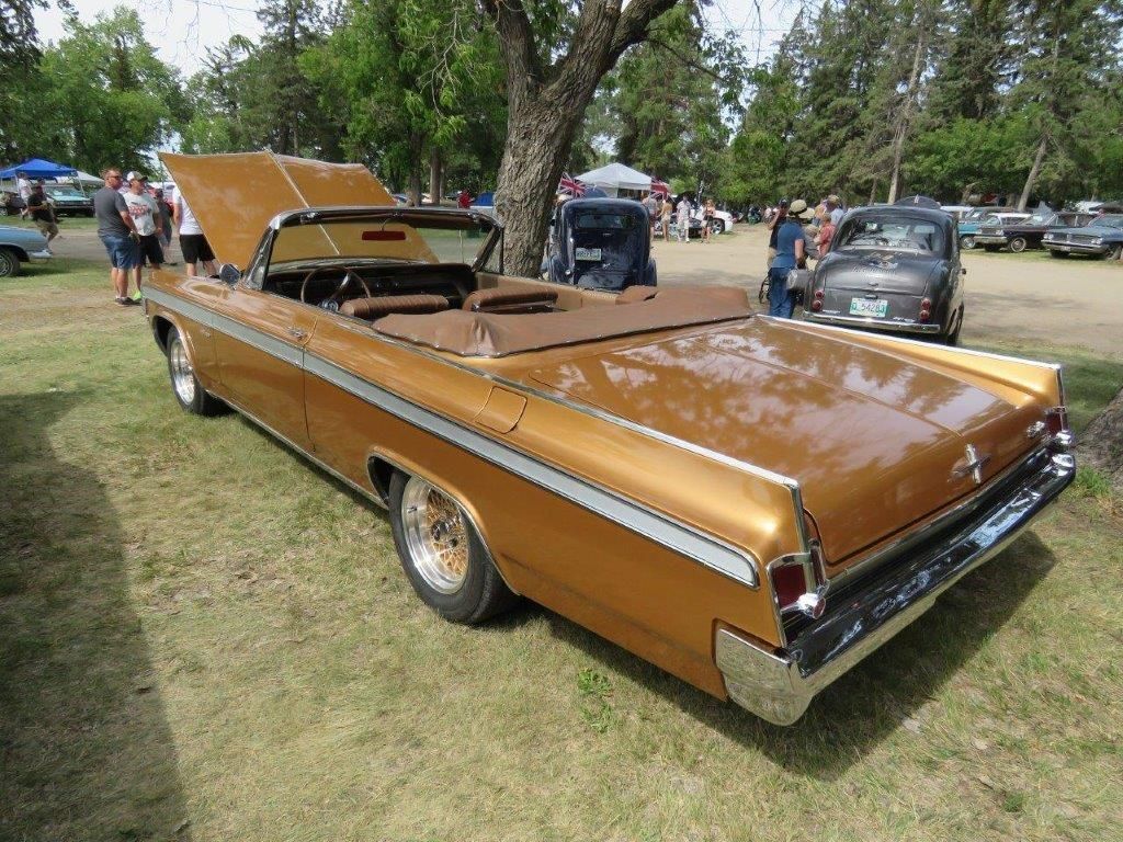 A gold convertible car with the hood up is parked in a grassy field.