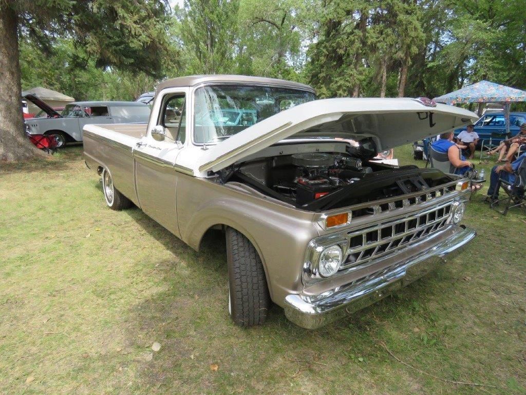 A truck with the hood up is parked in the grass at a car show.