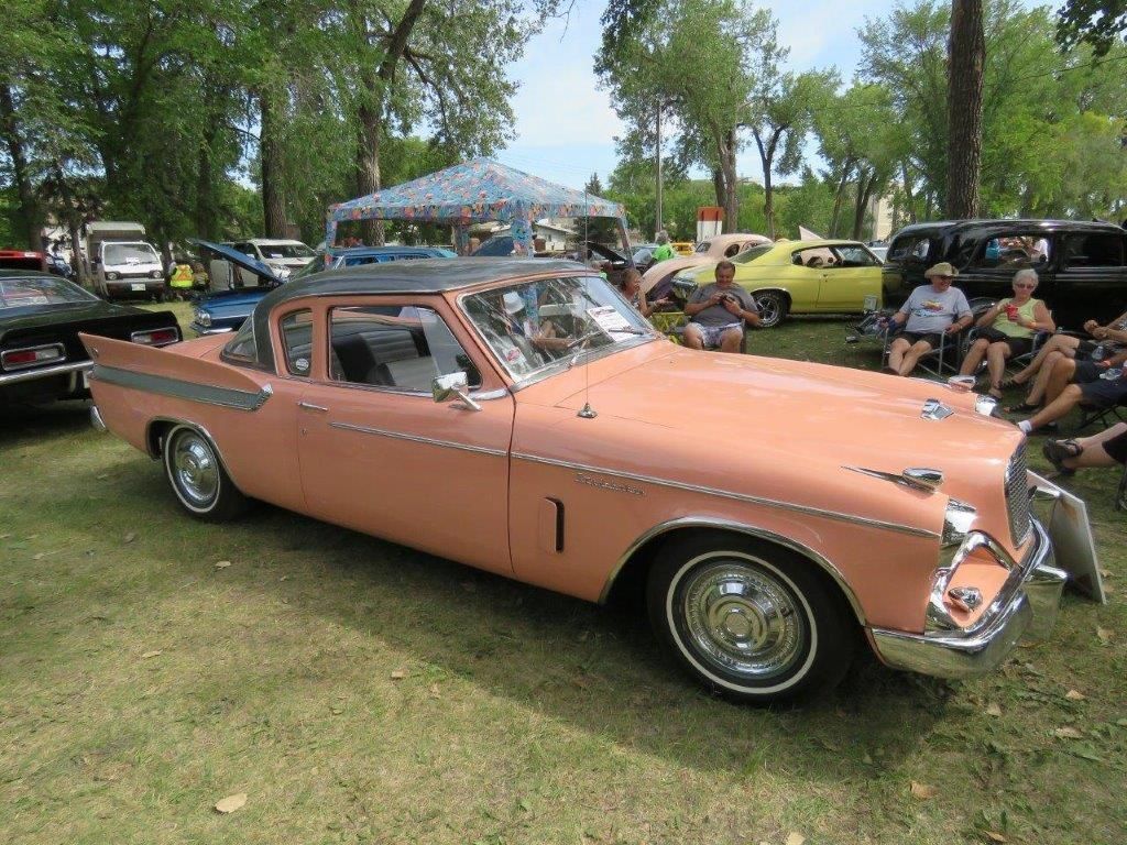A pink car is parked in the grass at a car show.