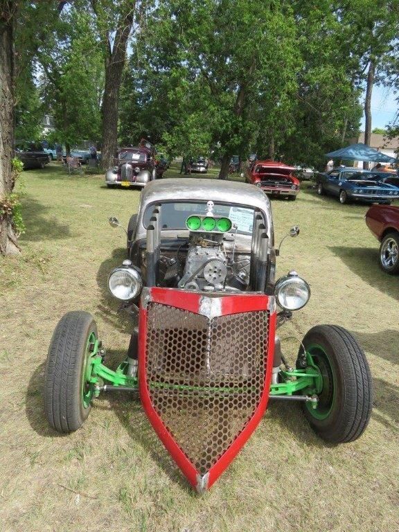 A car with a red grille and green wheels is parked in a grassy field