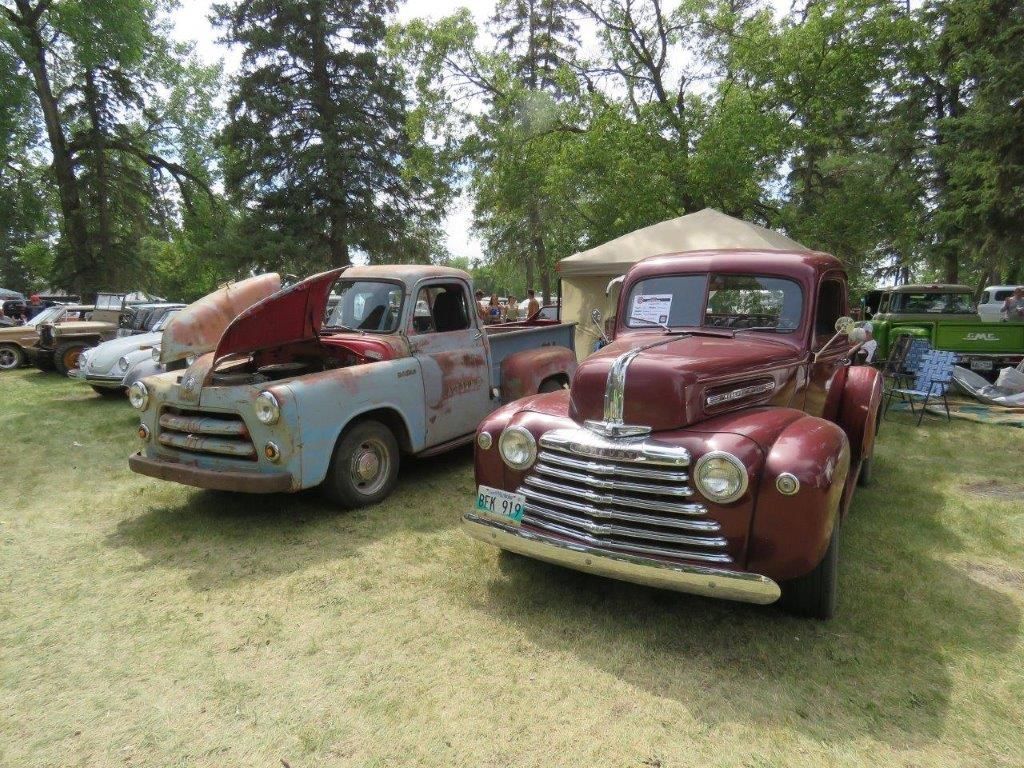 Two old trucks are parked next to each other on a grassy field.