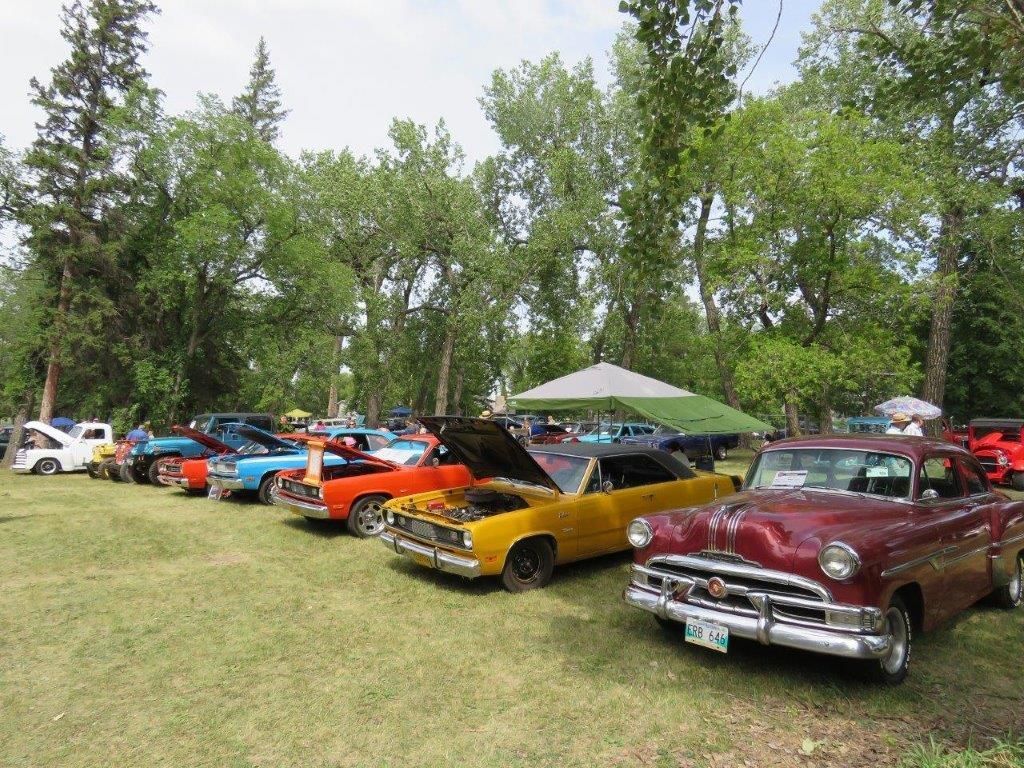 A row of old cars are parked in a grassy field.