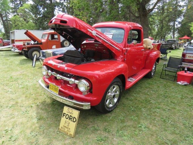 A red ford truck with the hood up is parked in a grassy field.