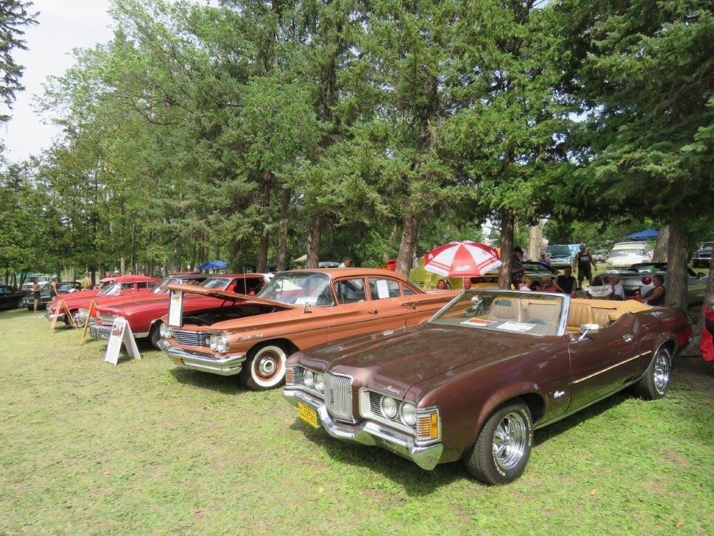 A row of old cars are parked in a grassy field.