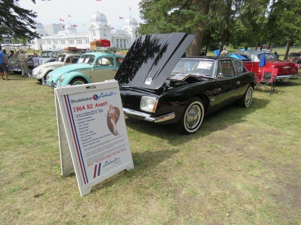 A black car with the hood up is parked next to a sign.