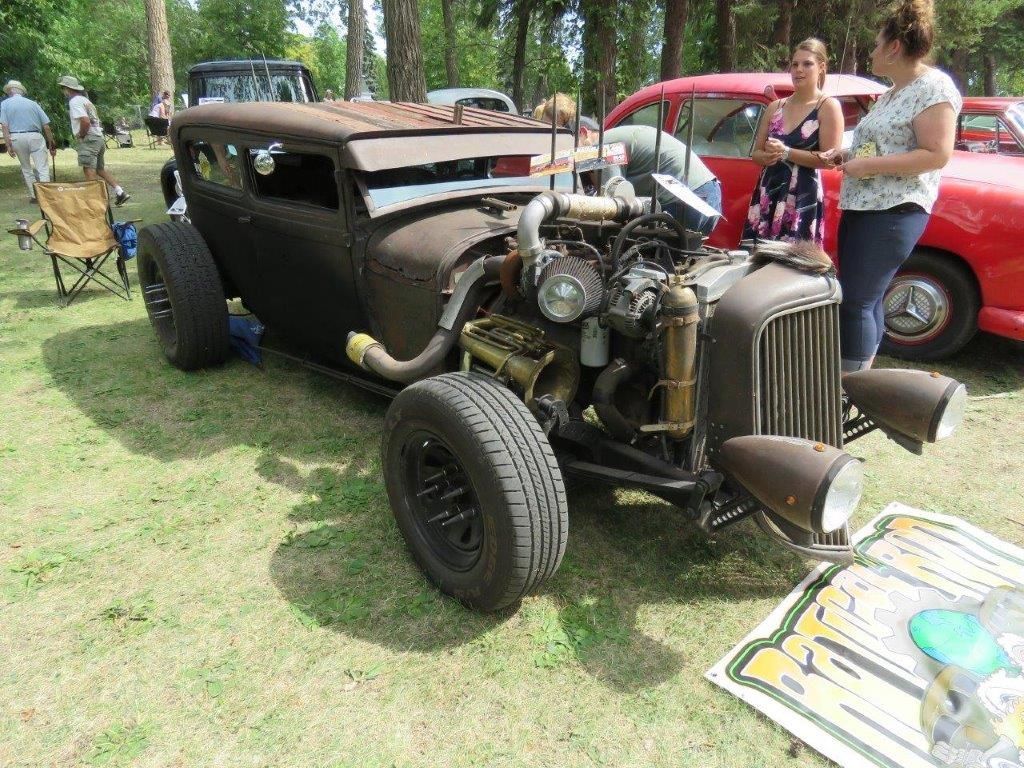A woman is standing next to a rusty old car at a car show.