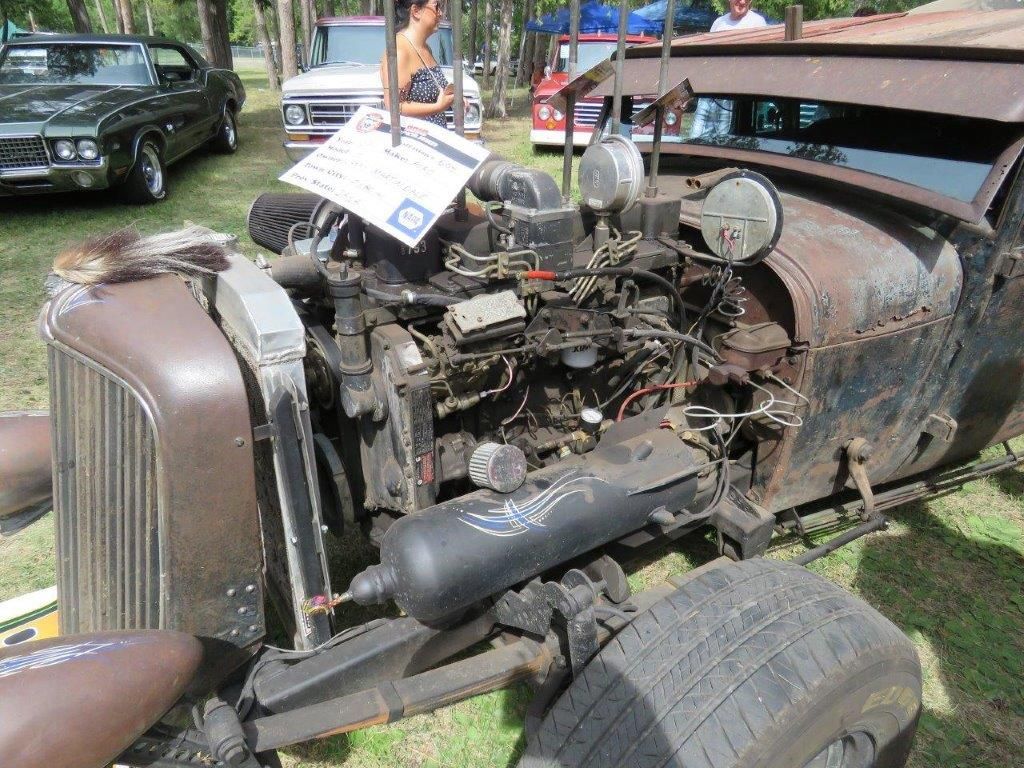 An old rusty car with the engine exposed is parked in the grass.