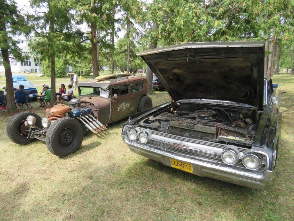 Two old cars are parked next to each other in a grassy field.