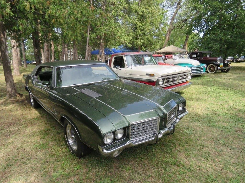 A green car is parked next to a white car in a grassy field.