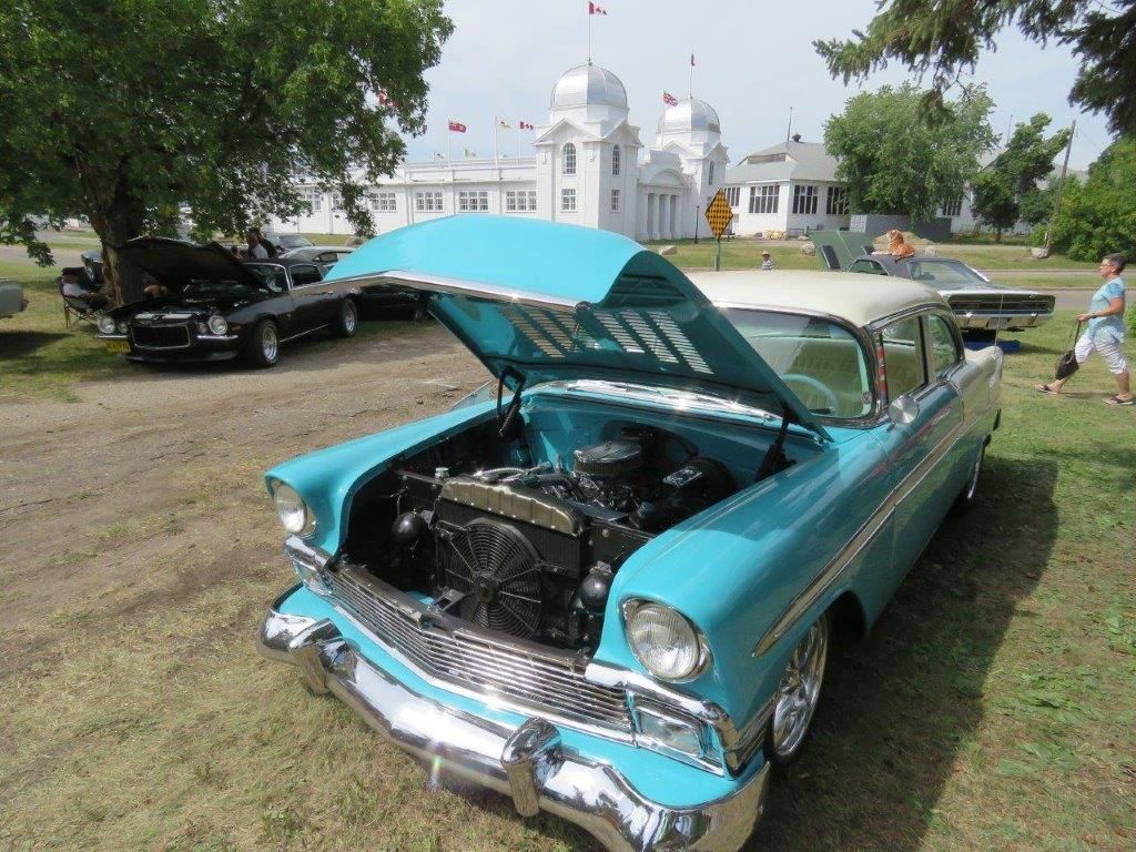 A blue car with the hood up is parked in a grassy field