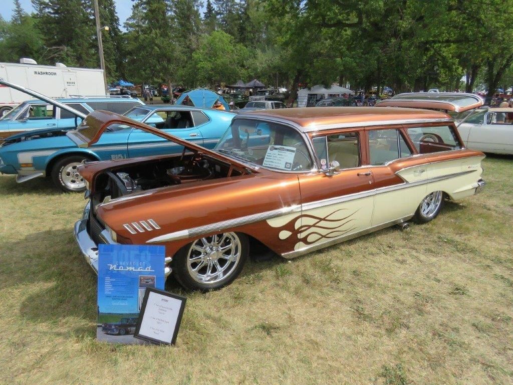 A brown and white station wagon is parked in the grass at a car show.