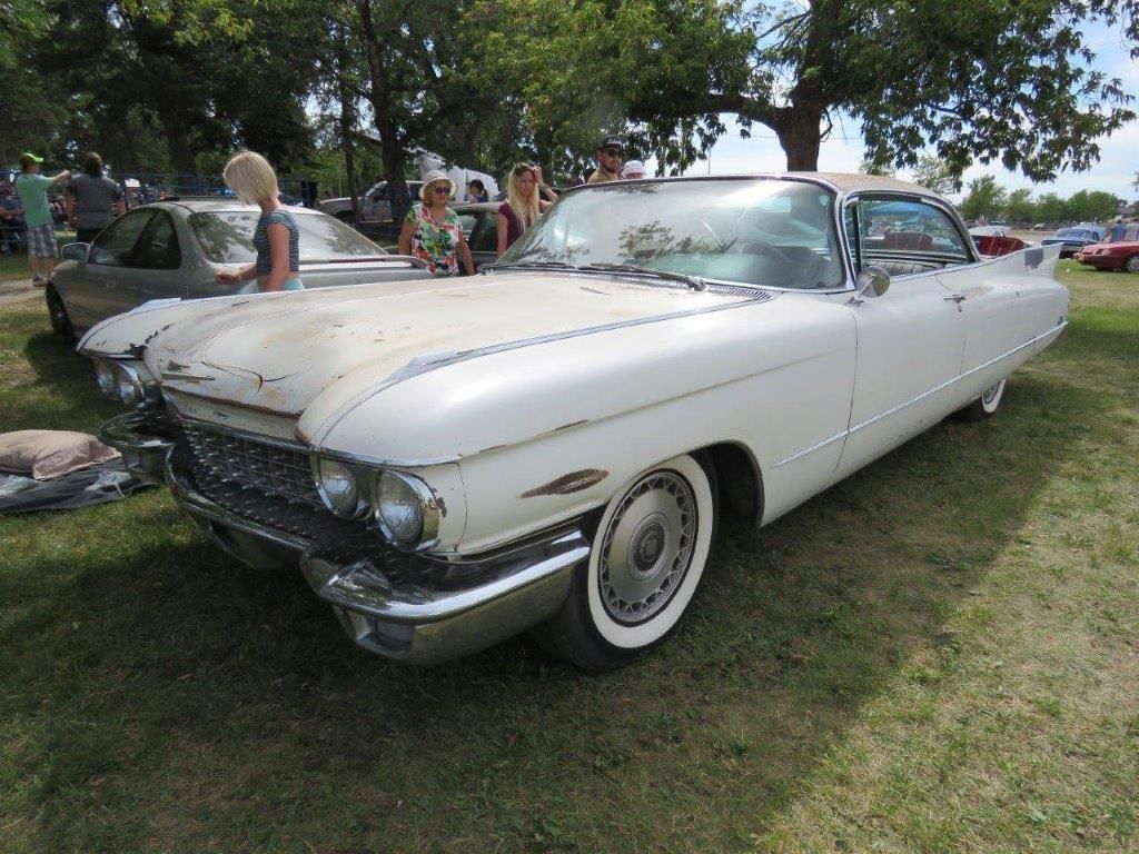 A white cadillac is parked in the grass at a car show.