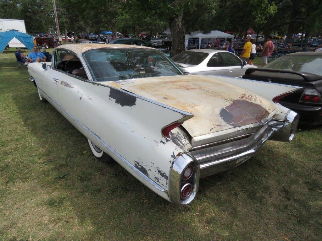 A white cadillac is parked in the grass at a car show.