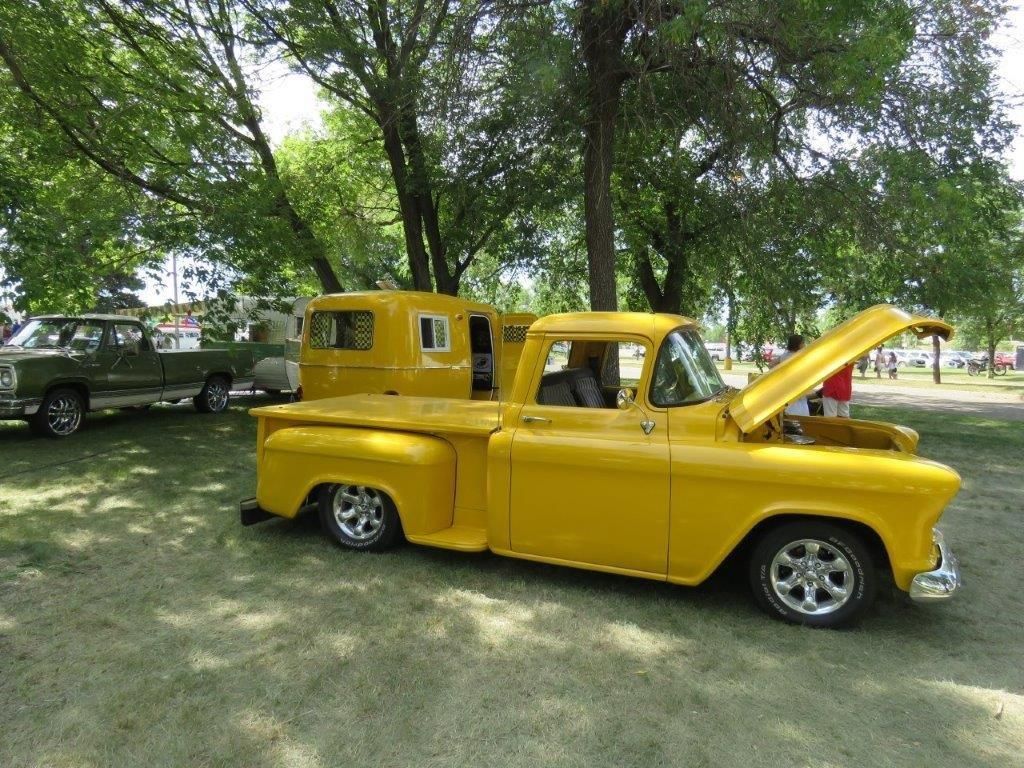 A yellow truck with the hood up is parked in a park.