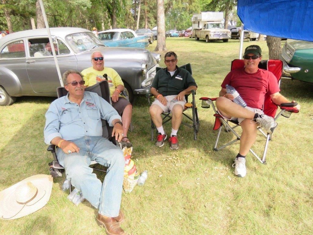 A group of men are sitting in chairs in front of a car.
