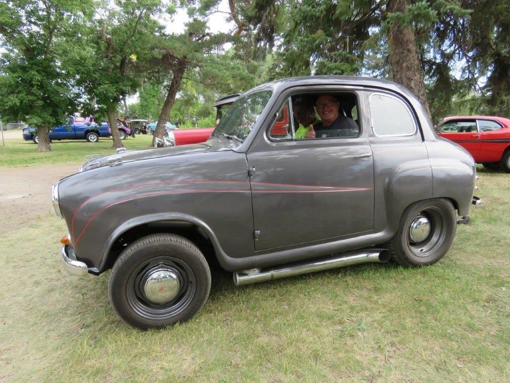 A man is sitting in an old car parked in the grass.