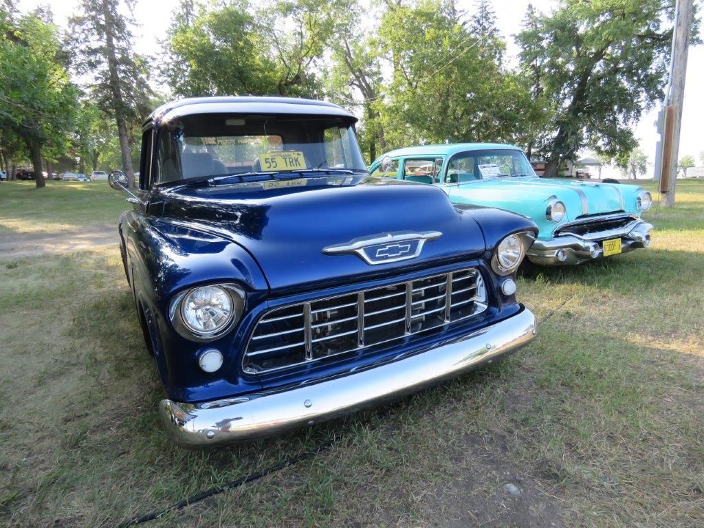 Two old trucks are parked next to each other in a grassy field.