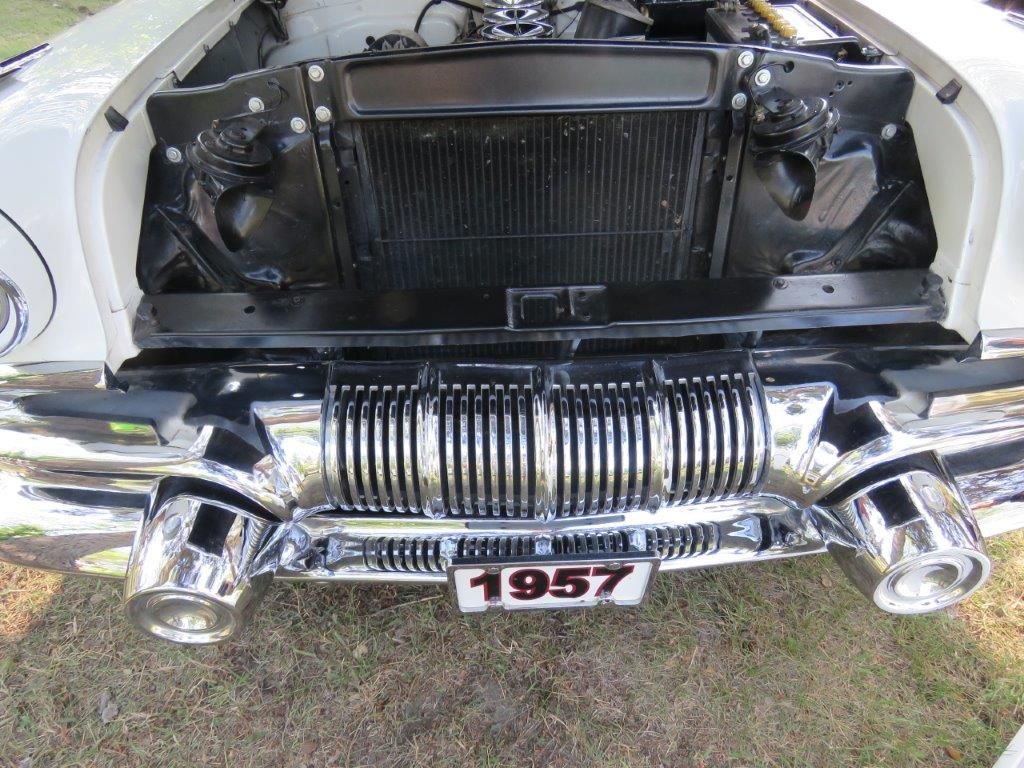 A white car with the hood open and a license plate that says 1957