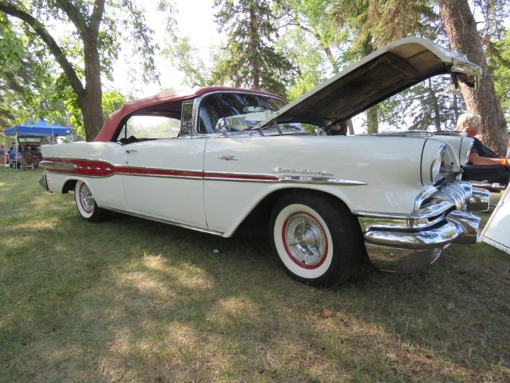 An old white car with the hood up is parked in the grass.
