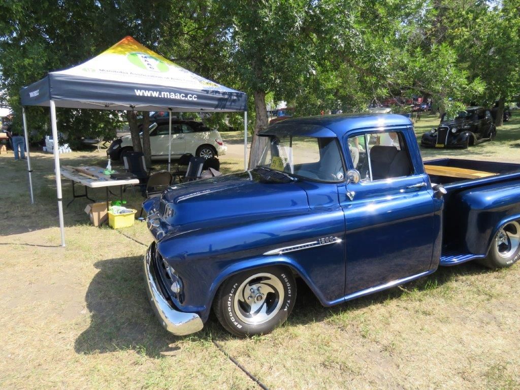A blue truck is parked in a grassy field next to a tent.