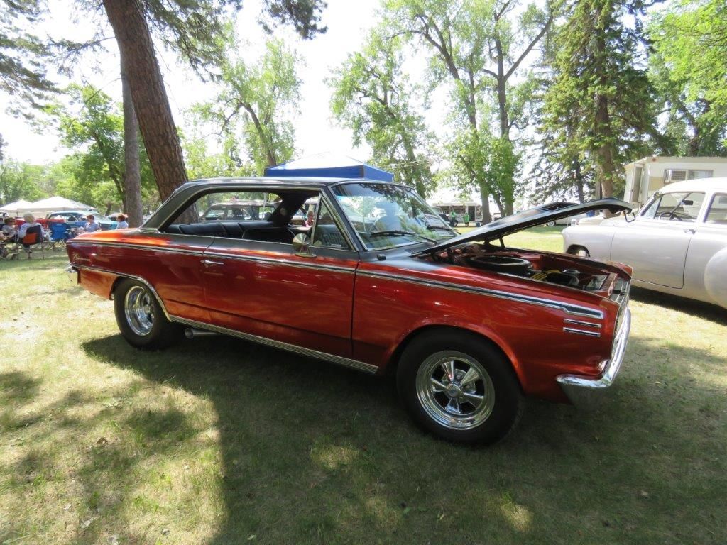 A red car with the hood up is parked in a grassy field.
