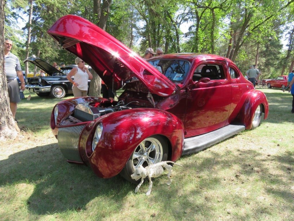 A red car with the hood up is parked in a grassy field.