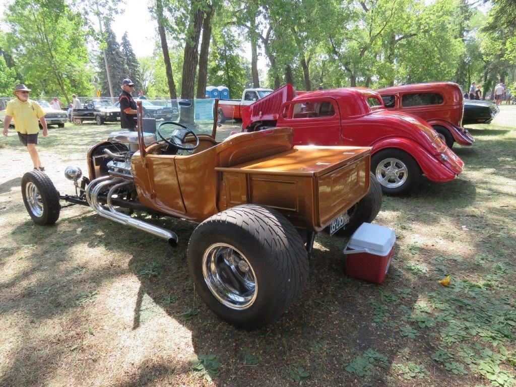 A wooden hot rod is parked next to a red car at a car show.