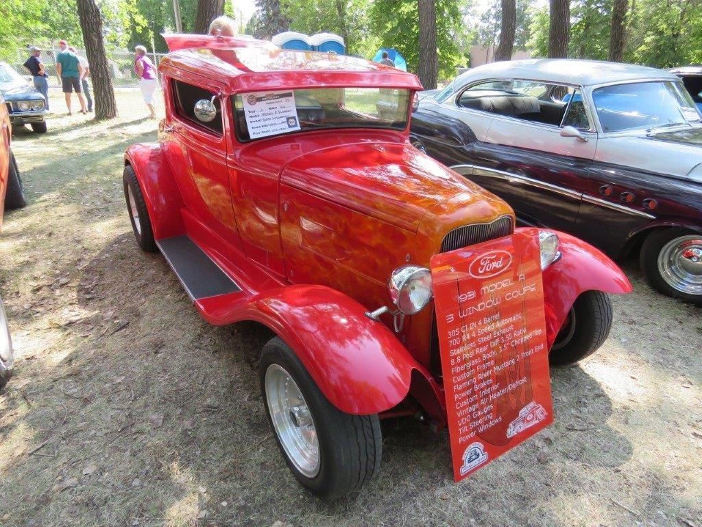 A red car with a wooden body is parked next to a black car at a car show.