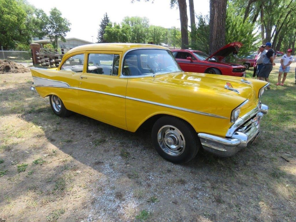 A yellow car is parked in a dirt field next to a red car.