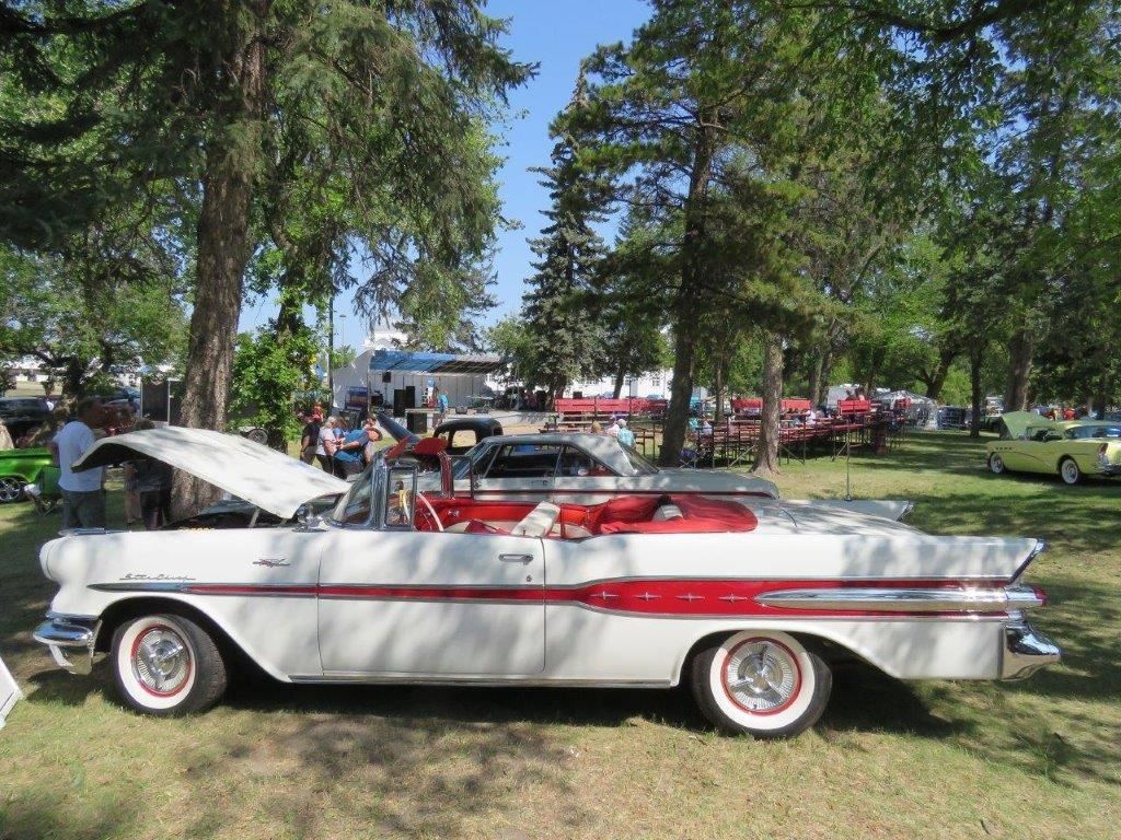 A white and red car with the hood up is parked in a park.