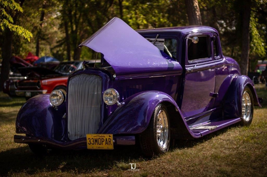 A purple car with the hood up is parked in the grass.