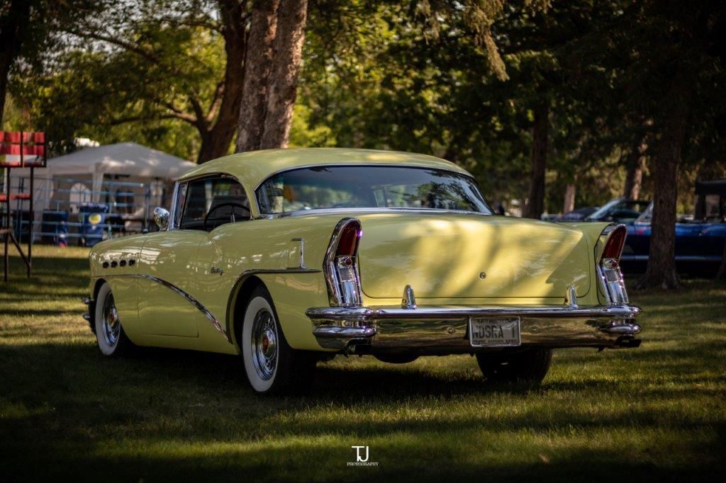 A yellow car is parked in the grass in a park.